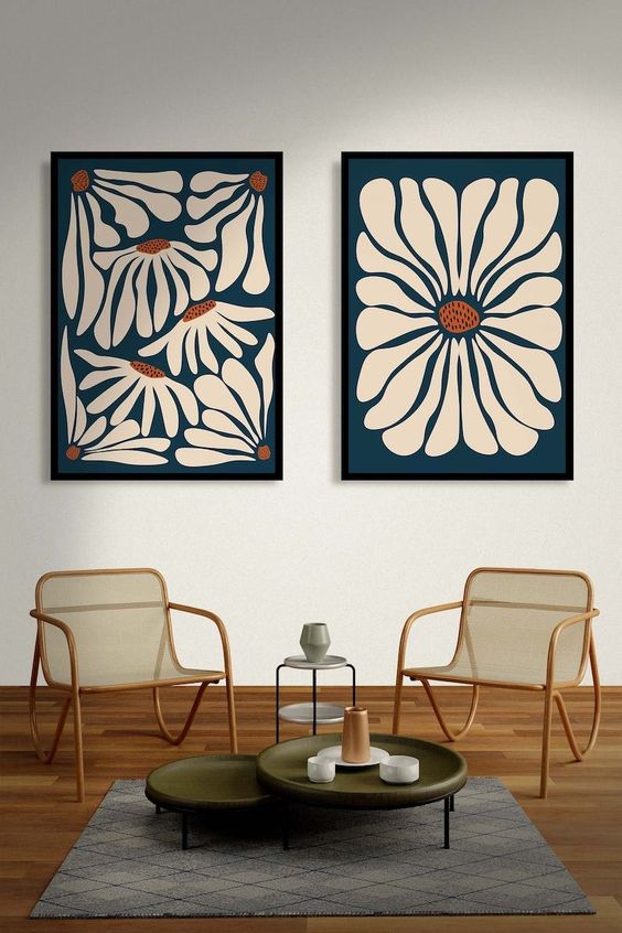Two wooden chairs and a table in front of a white wall with two large blue images on it.